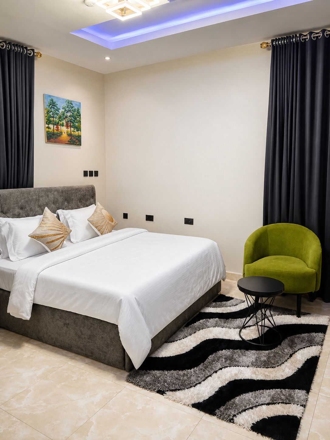 Un dormitorio con una cama, un sillón verde, una alfombra y un cuadro en la pared.