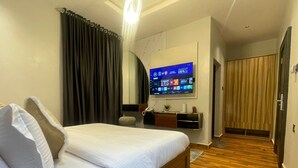 A hotel room with a bed, a desk, a TV, and a wooden floor. - The Address 127 - Refined Apartments (Abuja)