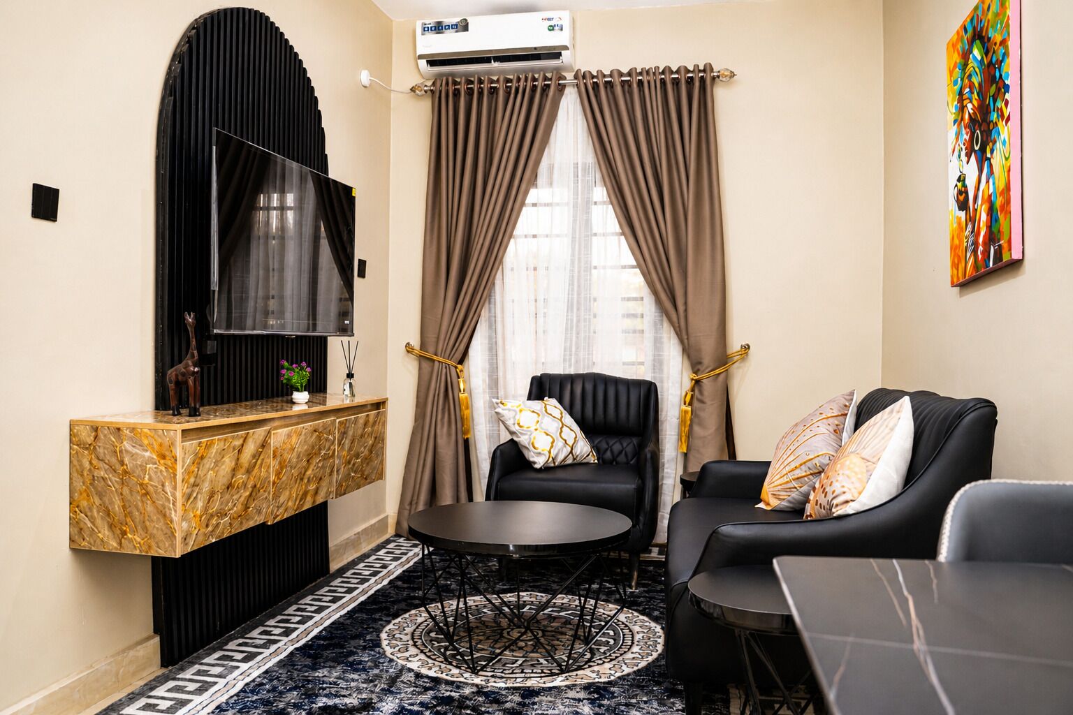 A compact living space with a marble console, a black leather sofa, a round table, and a television.