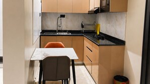 A compact kitchen with a dining area, a microwave, a sink, and a trash bin. - The Address 127 - Refined Apartments (Abuja)