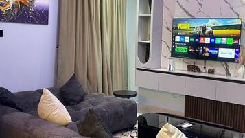 Una sala de estar moderna con un sofá seccional, un televisor de pantalla plana y una unidad de pared con diseño de mármol.