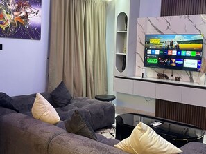 Una sala de estar moderna con un sofá seccional, un televisor de pantalla plana y una unidad de pared con diseño de mármol.