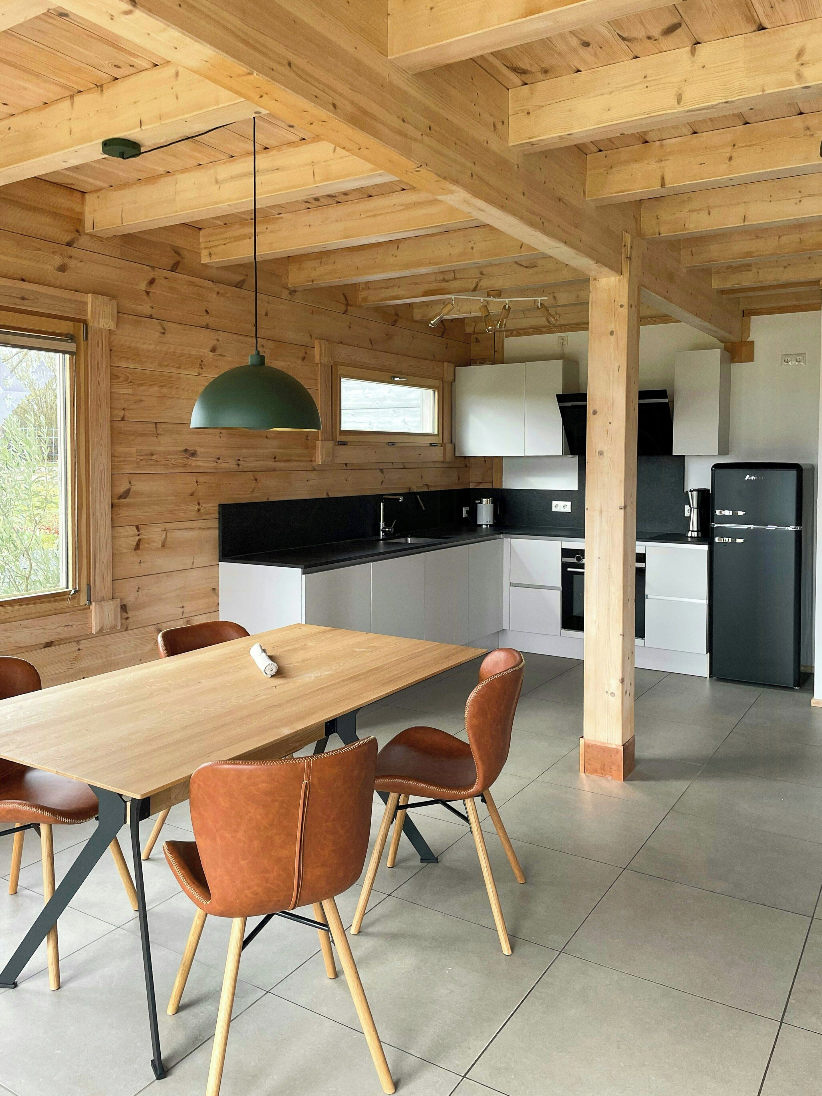 A modern kitchen with wooden beams, a dining table with chairs, and built-in appliances.