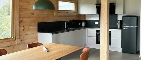 A modern kitchen with wooden beams, a dining table with chairs, and built-in appliances.