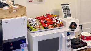Una zona de cocina con microondas, dispensador de agua y una presentación de fideos instantáneos.
