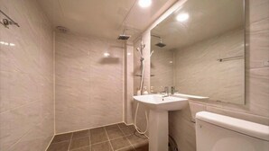 Baño con ducha, lavamanos, inodoro y un espejo grande.