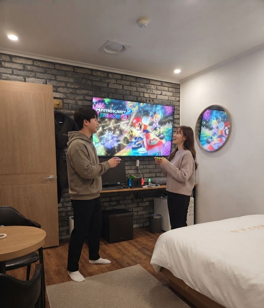 A room with a brick wall, a television displaying a game, a bed, and a round mirror.
