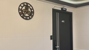 Una habitación con una puerta negra con el número '401', un sofá de cuero marrón, un reloj de pared y una lámpara en el techo.