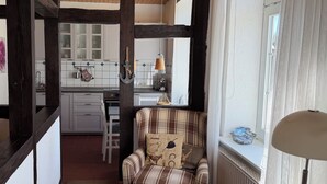 A cozy room with a wooden ceiling, a plaid sofa, a window with curtains, and a kitchen area in the background. - "Sonneneck" - Garden view, half-timbered, 37 m², sleeps 2, dogs welcome (Bösdorf)