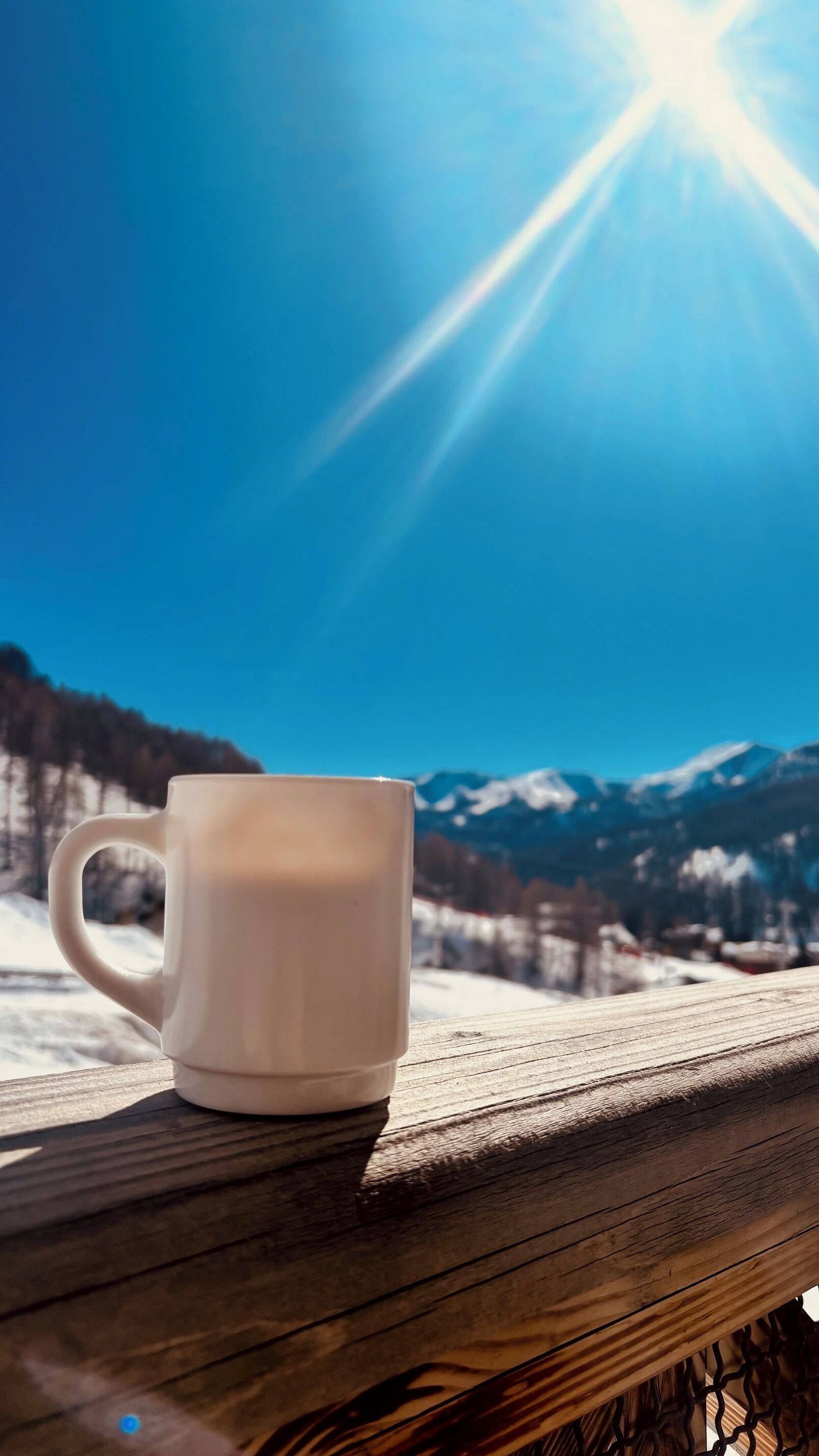 A white mug on a wooden railing with a mountain landscape and clear sky in the background.