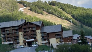 Ein mehrstöckiges Hotel mit Balkonen, im Hintergrund eine Skipiste und ein klarer Himmel.