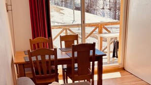 Ein gemütliches Zimmer mit einer Couch, einem Esstisch mit Stühlen und Blick auf eine verschneite Landschaft.