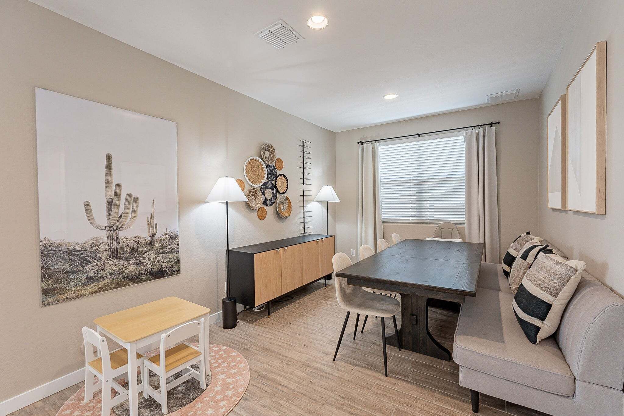 A dining area with a table, chairs, a sofa, a cabinet, and wall art.