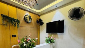 Un área de recepción con diseño moderno, que incluye un mostrador de recepción, un reloj, un televisor y una lámpara decorativa.