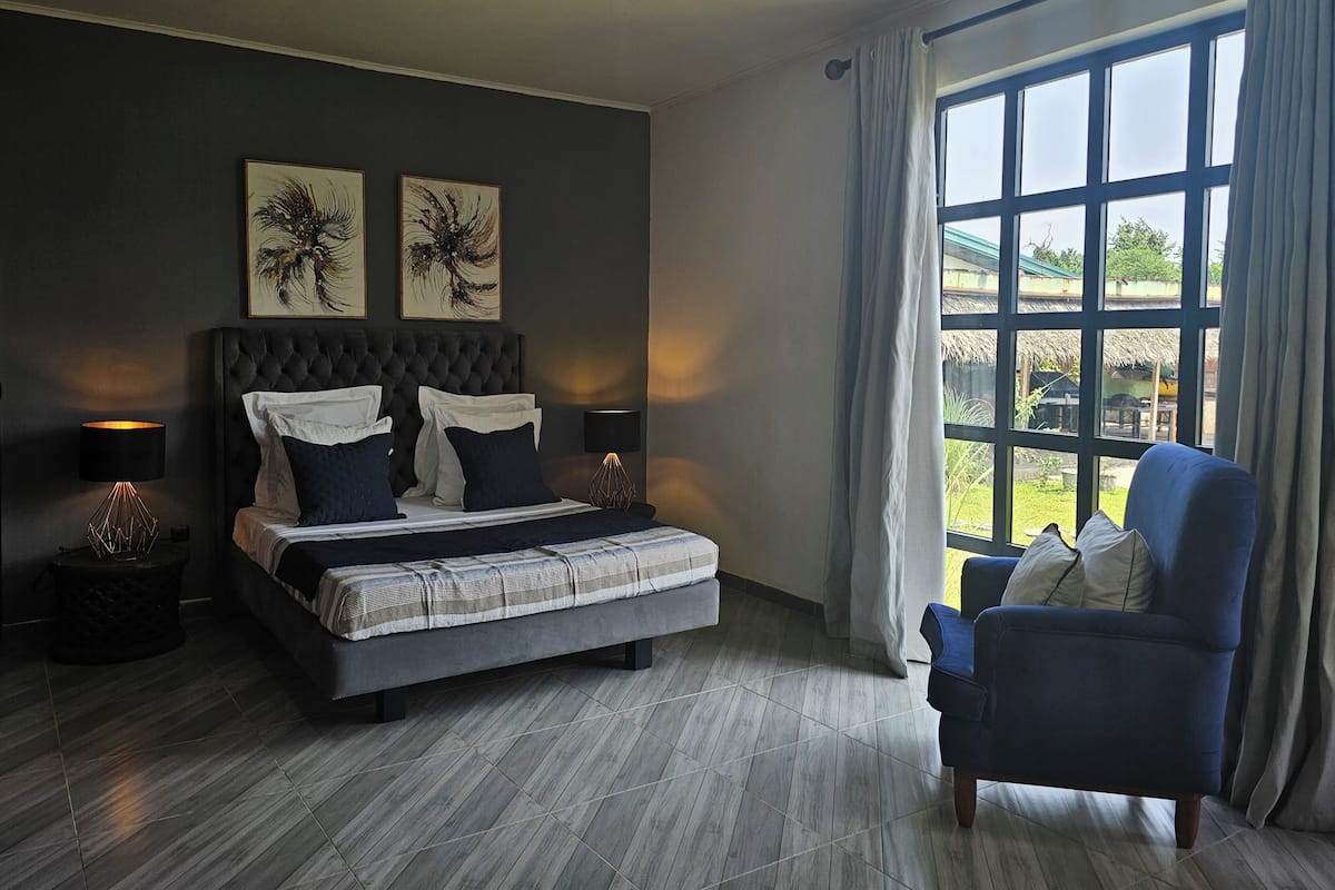 Un dormitorio con una cama grande, una silla, una ventana con cortinas y una obra de arte en la pared.
