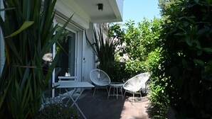 En patio med hvide stole og et bord, omgivet af frodig vegetation.