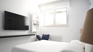 Et soveværelse med seng, fjernsyn monteret på væggen, et vindue og en radiator.