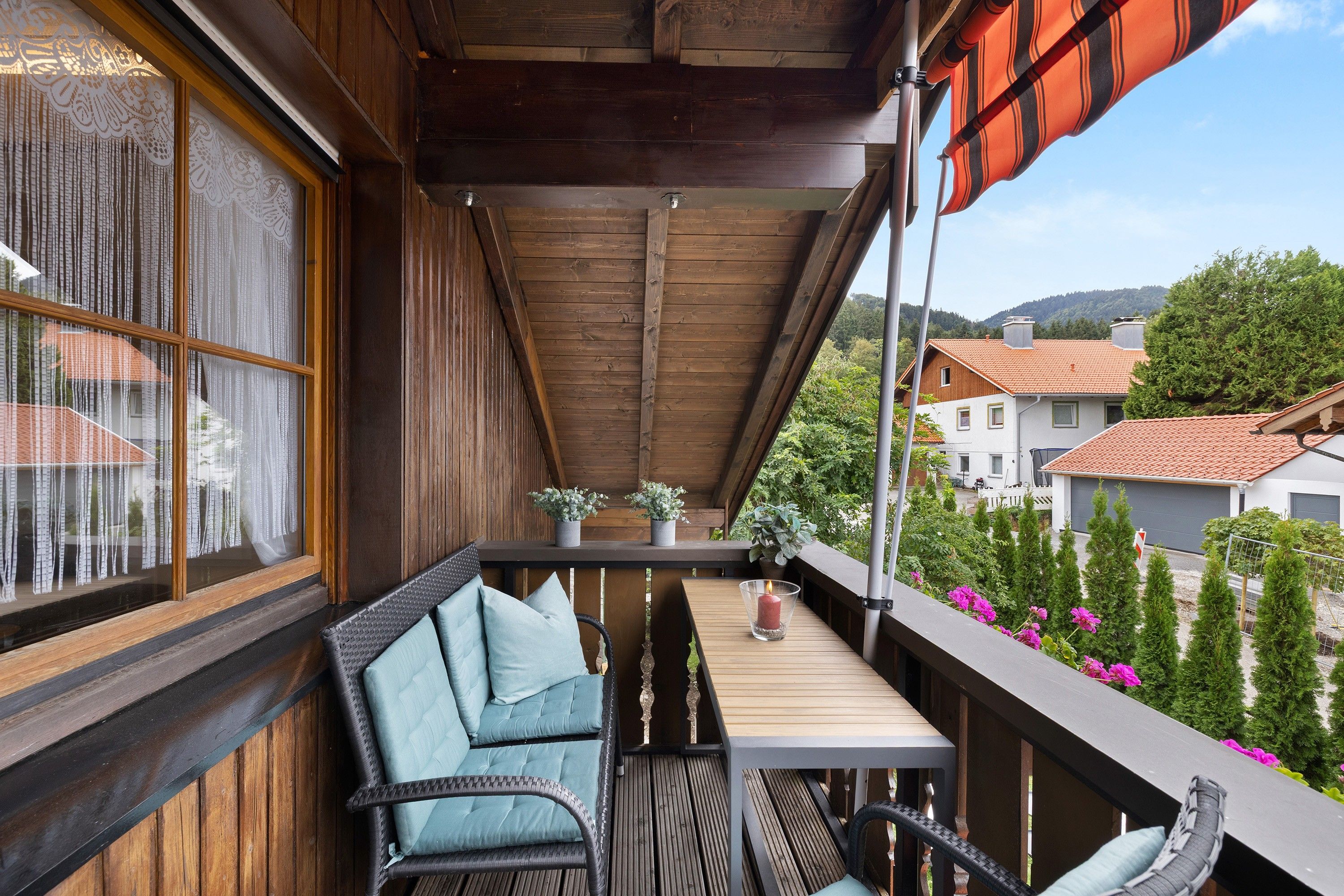Ein hölzerner Balkon mit Tisch, Stühlen und Blumentöpfen.