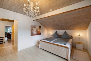 Un dormitorio con techo de madera, una araña, una cama con almohadas, un cuadro en la pared y una mesita de noche.