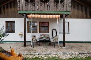 Un espacio al aire libre techado con mesa y sillas, una maceta colgante y un banco de madera.