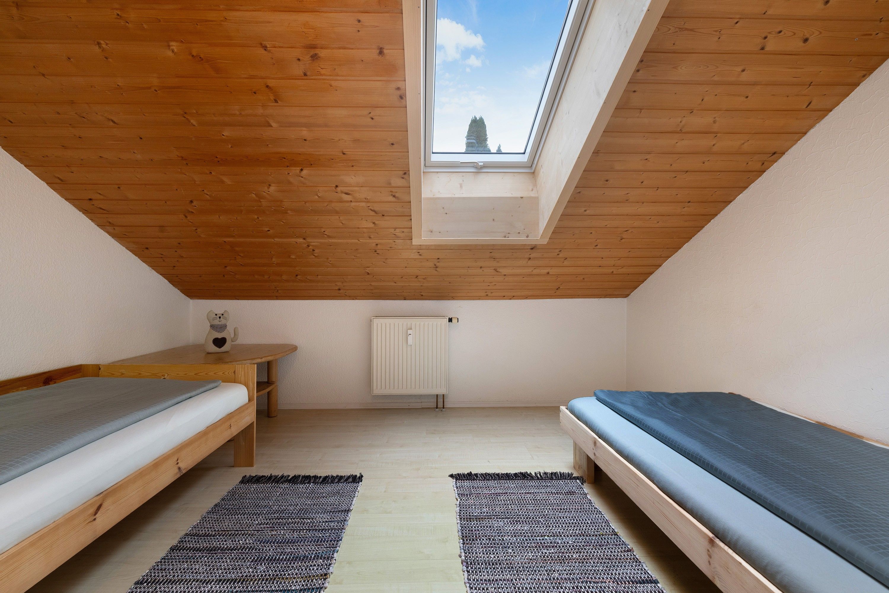 Une petite pièce avec un toit en pente, deux lits, un radiateur et une lucarne.