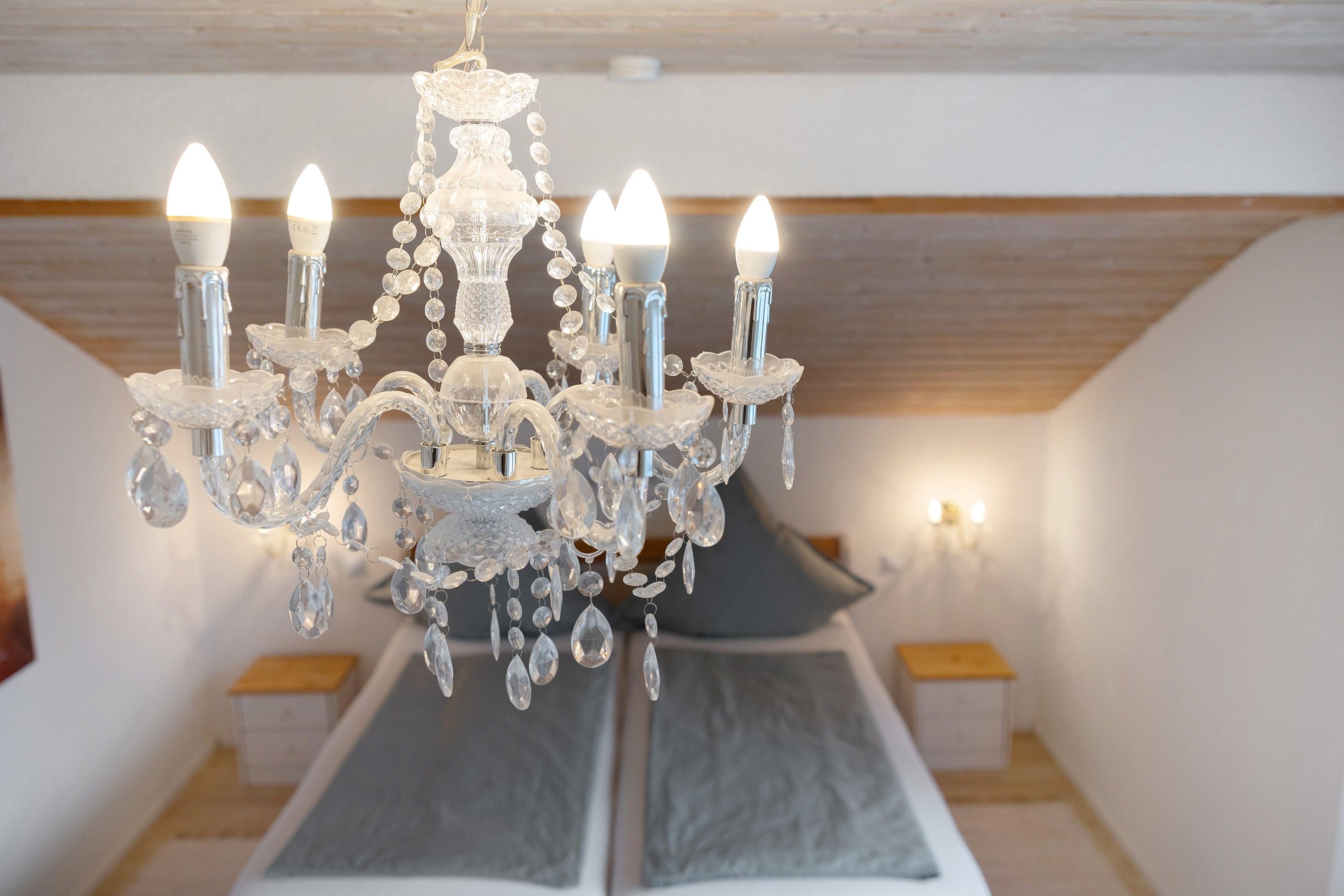 A chandelier with multiple lights in a room with a bed and a wall-mounted light.