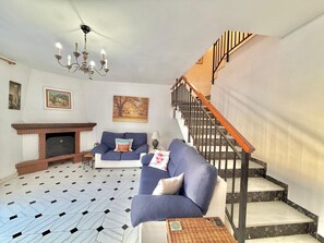 Una sala de estar con chimenea, un sofá, una mesa de centro, una escalera y una araña.