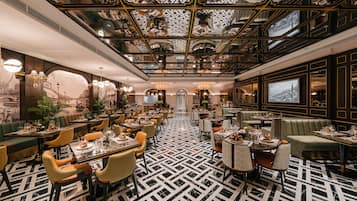 A spacious dining area with high ceilings and ornate ceiling decorations, featuring multiple dining tables and chairs.