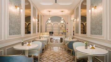 Een hotelentree met ronde tafels, blauwe fauteuils, behang met een patroon en een centraal presentatiegedeelte.