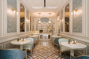 A hotel lobby with round tables, blue upholstered chairs, patterned wallpaper, and a central display area. - Classyc Hotel Hang Buom (Hanoi)
