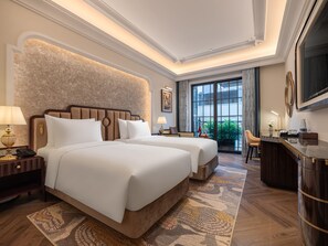 A hotel room with two beds, a desk, a chair, a TV, and a balcony with plants. - Classyc Hotel Hang Buom (Hanoi)