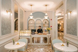 A hotel lobby with a reception desk, two round tables with chairs, and a display case with items. - Classyc Hotel Hang Buom (Hanoi)