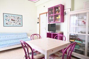 Une pièce comprenant un canapé, une table avec des chaises, un meuble rose et un meuble en verre contenant de la vaisselle.