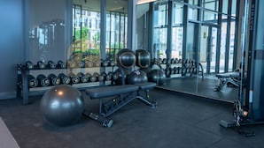 A gym with exercise equipment, a bench, and a mirror reflecting the room.