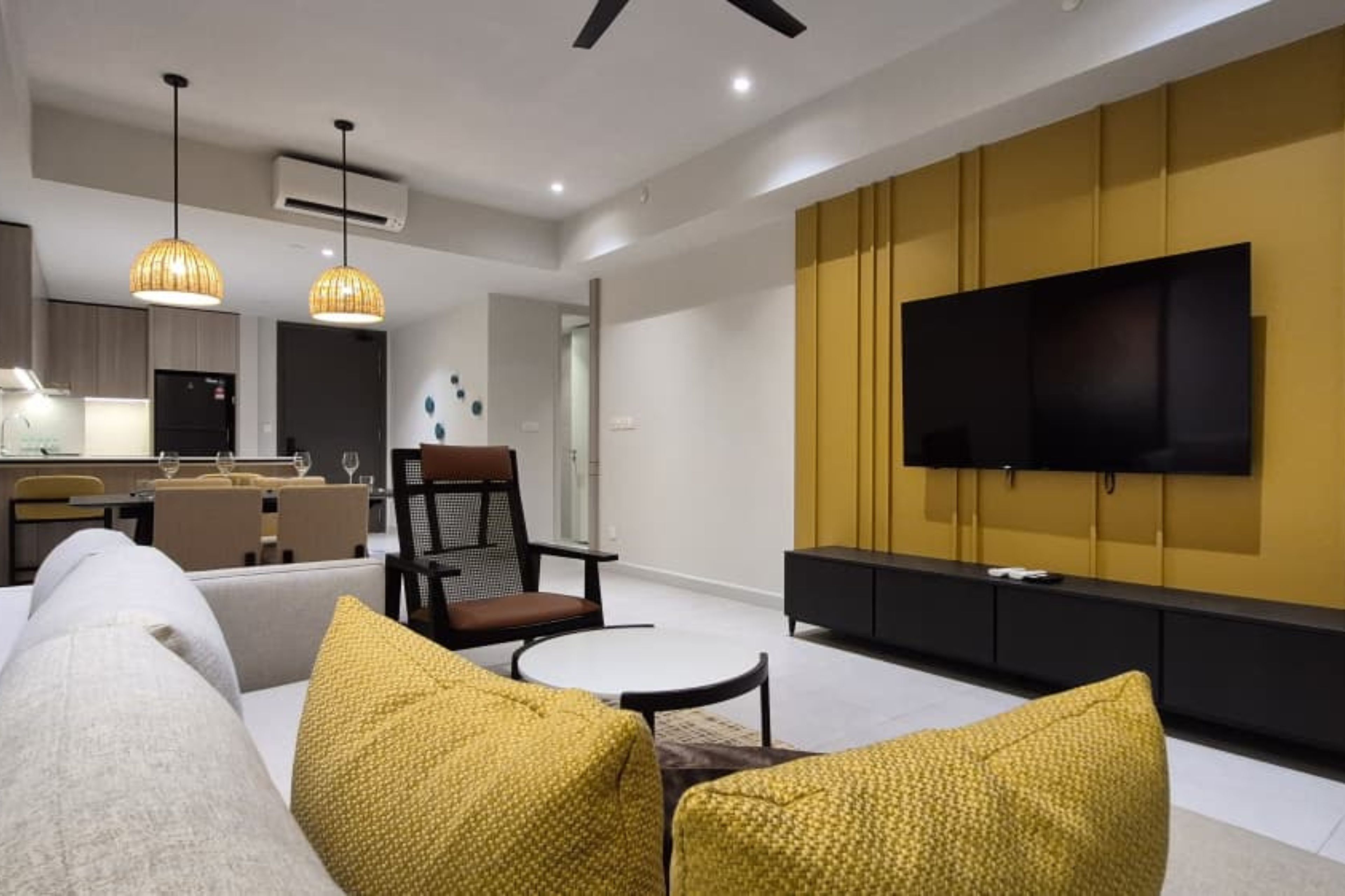 Een moderne zithoek met een bank, twee fauteuils, een salontafel en een flatscreen televisie bevestigd aan een gele muur.