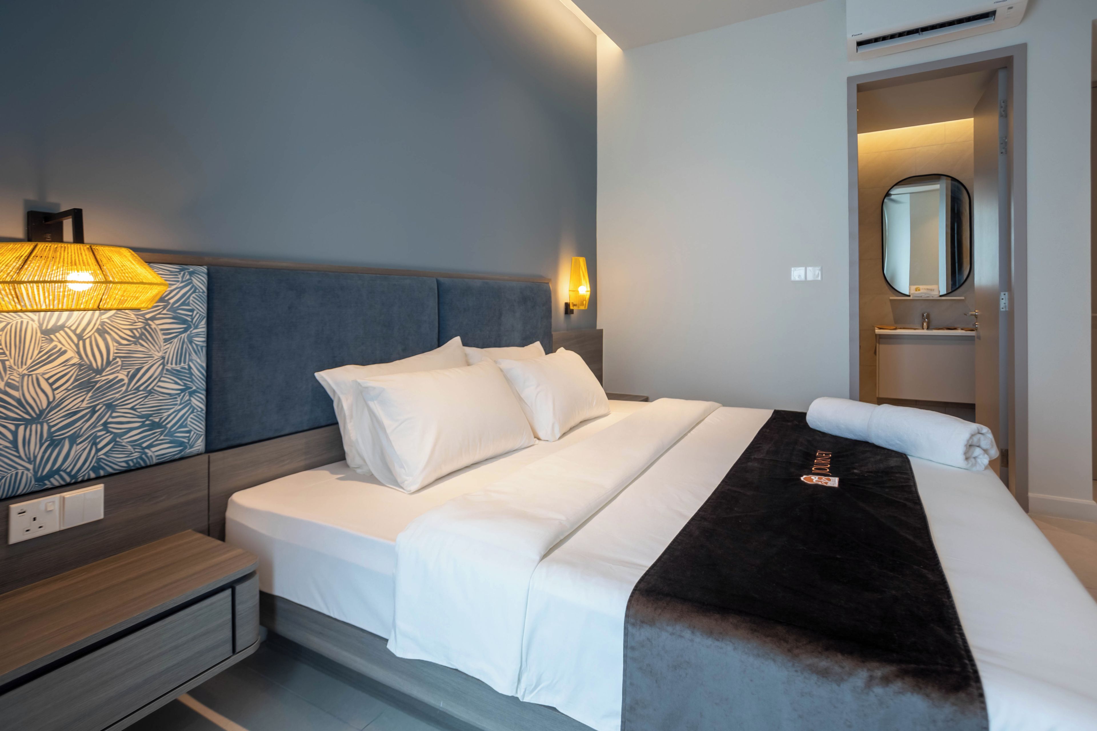 Una habitación de hotel con cama, mesita de noche, lámpara y espejo.