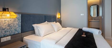 Una habitación de hotel con cama, mesita de noche, lámpara y espejo.