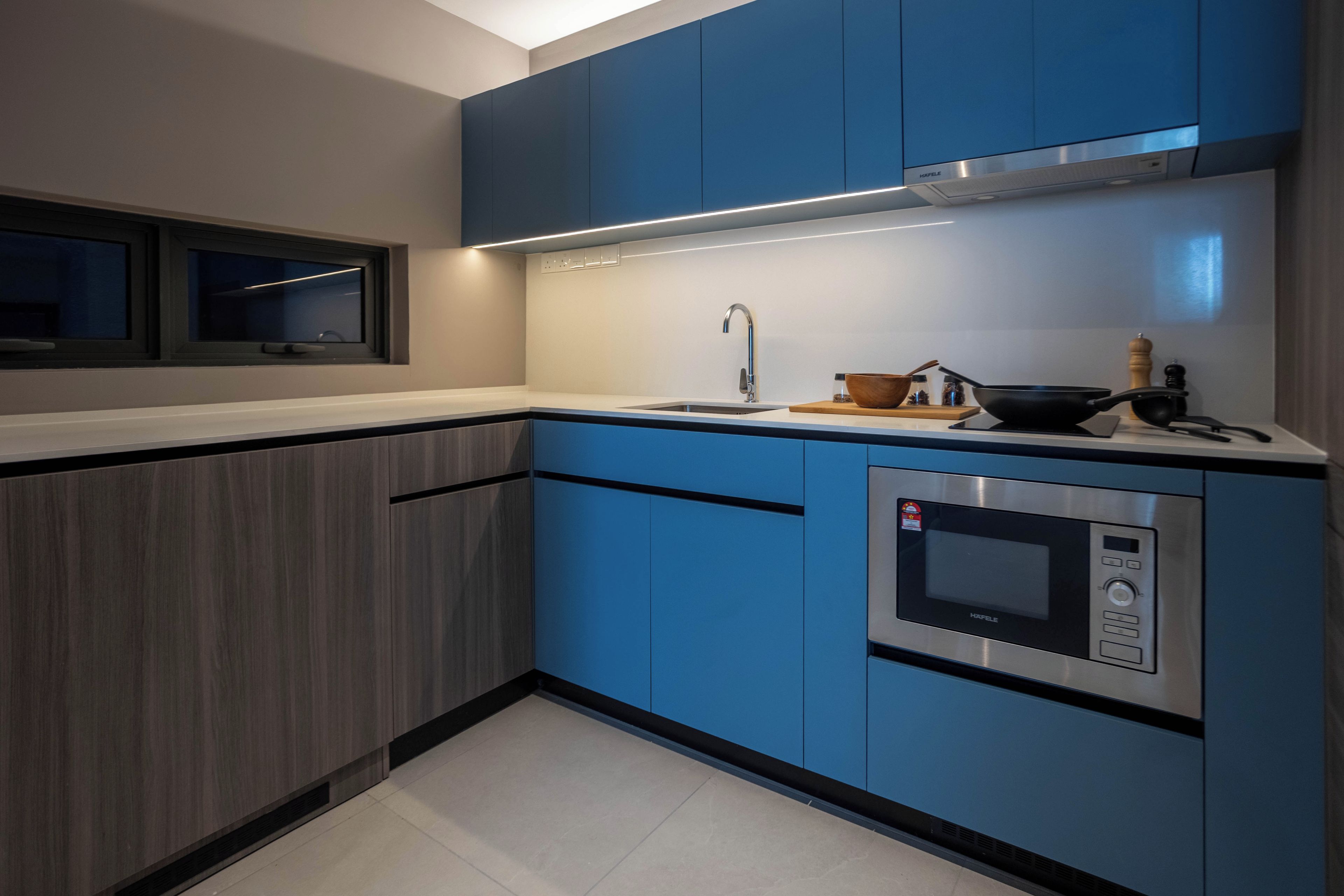 A modern kitchen with blue cabinets, a stainless steel microwave, and a window above the sink.