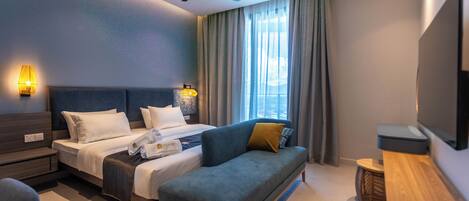 A modern hotel room with a bed, a sofa, a ceiling fan, and a TV.