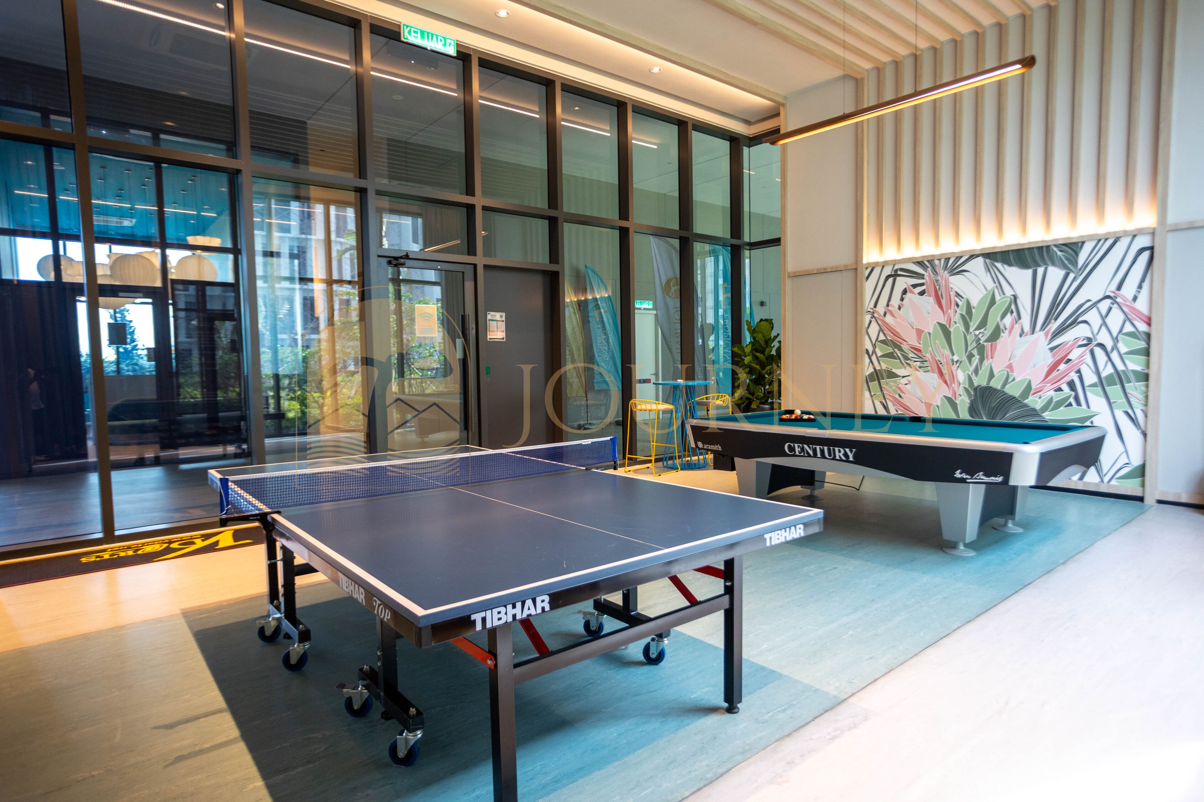 A billiards table and a ping pong table in a modern indoor setting with large windows and a tropical mural.