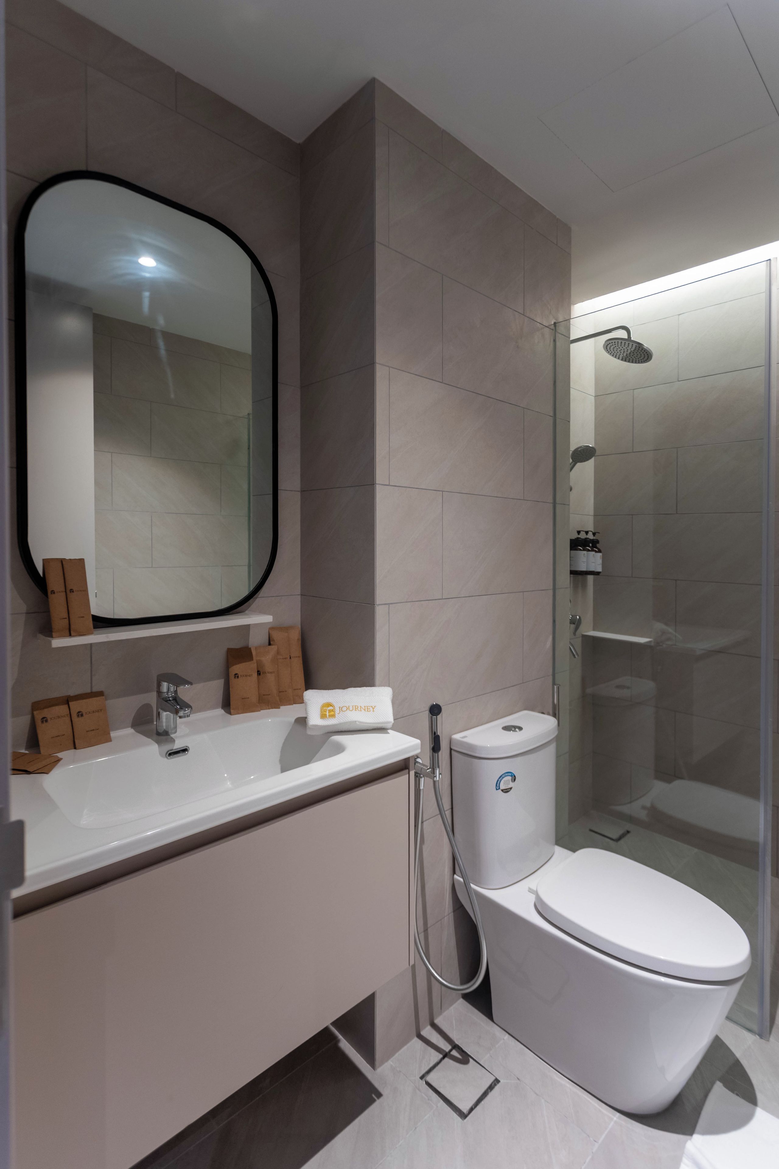 Een moderne badkamer met een witte wastafel, een grote spiegel, een douchecabine en een toilet.