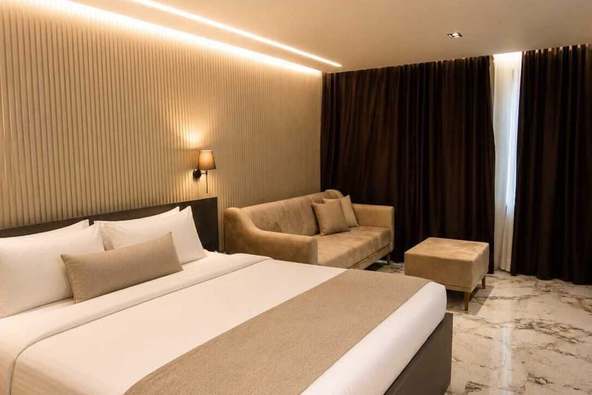 Une chambre d’hôtel moderne avec un grand lit, un canapé, une petite table et une lampe fixée au mur.