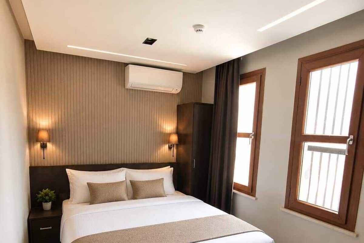 Une chambre à coucher moderne avec un grand lit, une table de chevet, un climatiseur fixé au mur et une fenêtre avec des rideaux.