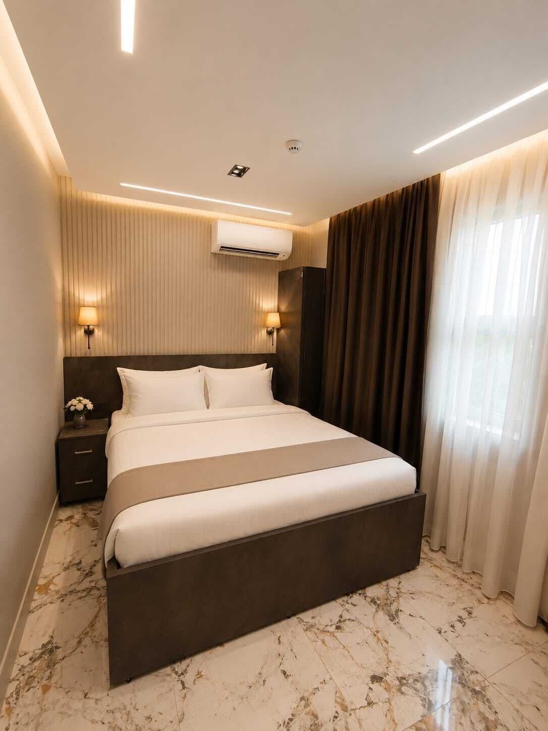 A modern hotel room with a large bed, a nightstand, an air conditioning unit, and a window with curtains.