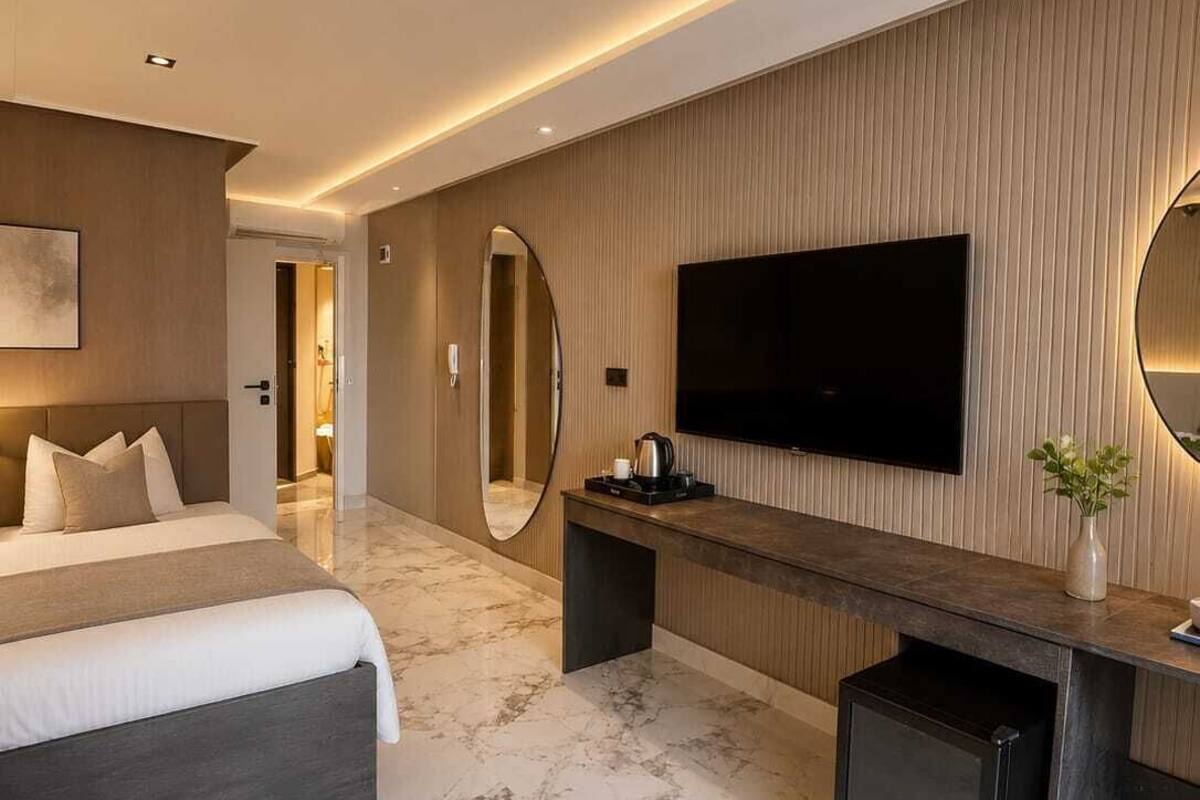 Une chambre d’hôtel moderne dotée d’un grand lit, d’un téléviseur à écran plat, d’une console et d’un sol en marbre.