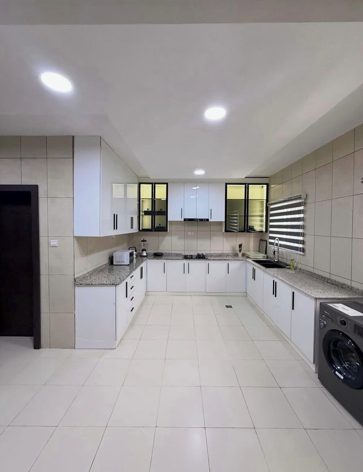 A modern kitchen with white cabinets, granite countertops, a built-in washing machine, and recessed ceiling lights.