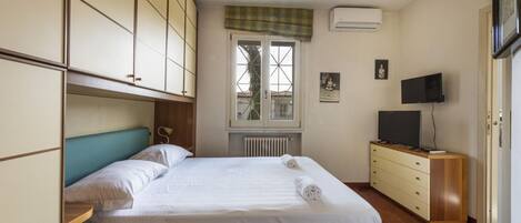 A bedroom with a bed, a television, a radiator, and a window with a view.