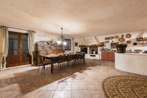 A spacious kitchen with a dining area, featuring a large wooden table and chairs, a built-in stove, and various kitchen utensils displayed on the wall. - Villa Camillo by MMega (Forte dei Marmi)