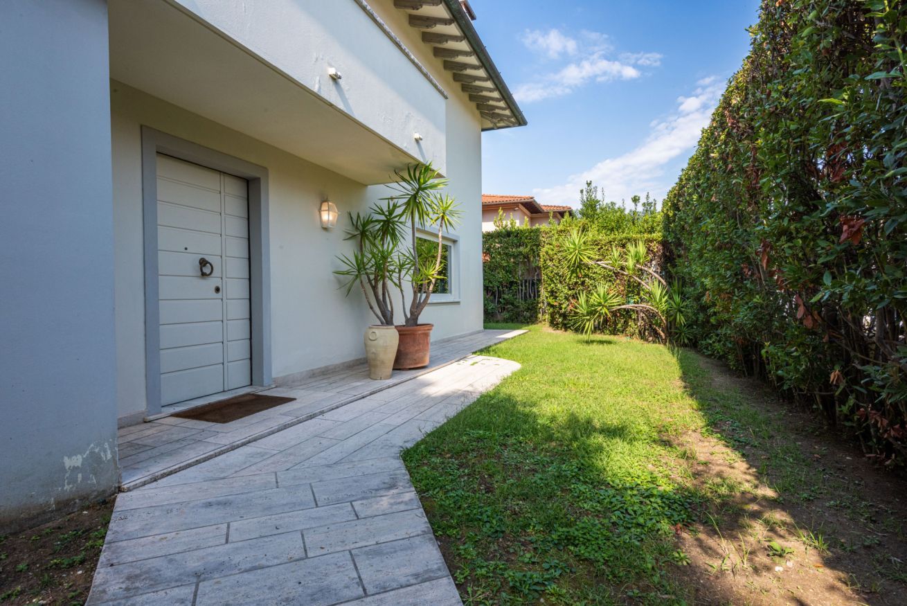 A modern house with a white exterior, a garage door, and a paved driveway leading to a well-maintained lawn.