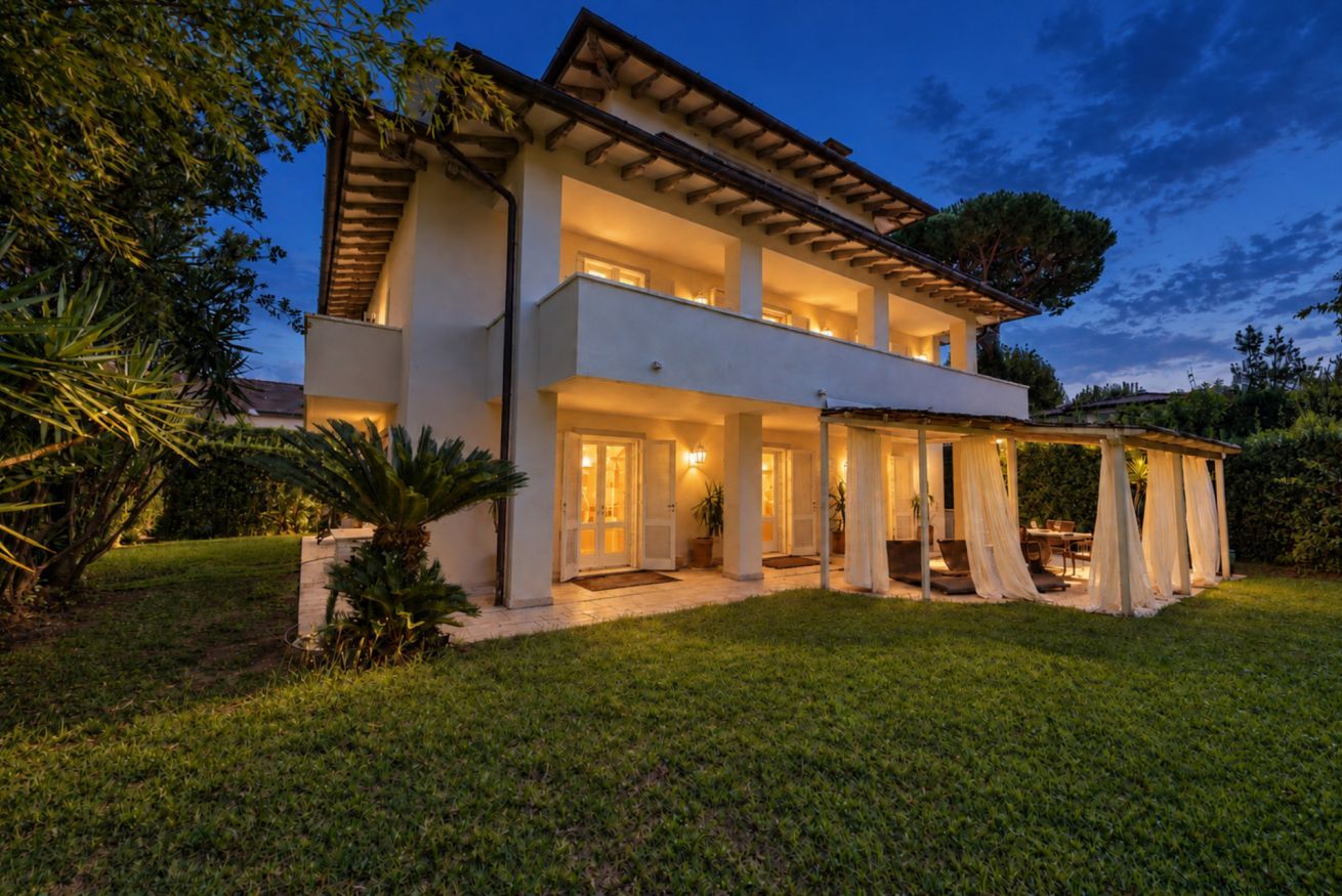 A two-story modern house with a covered patio and a well-maintained lawn.